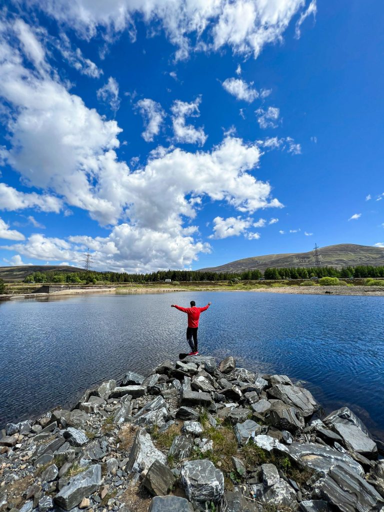 una persona parada sobre rocas junto a un cuerpo de agua